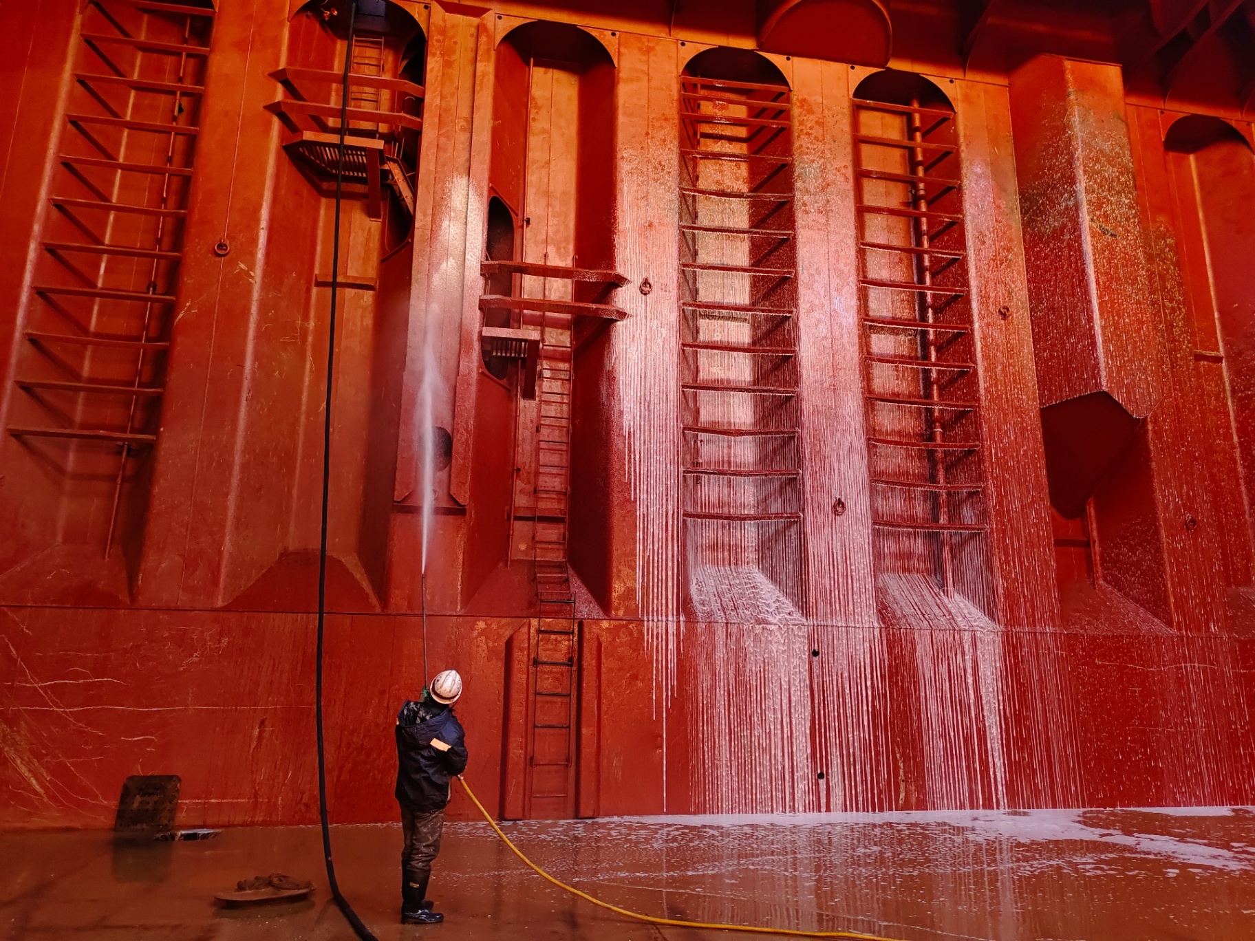 Marine inspector pressure-washing the red interior wall of a cargo hold