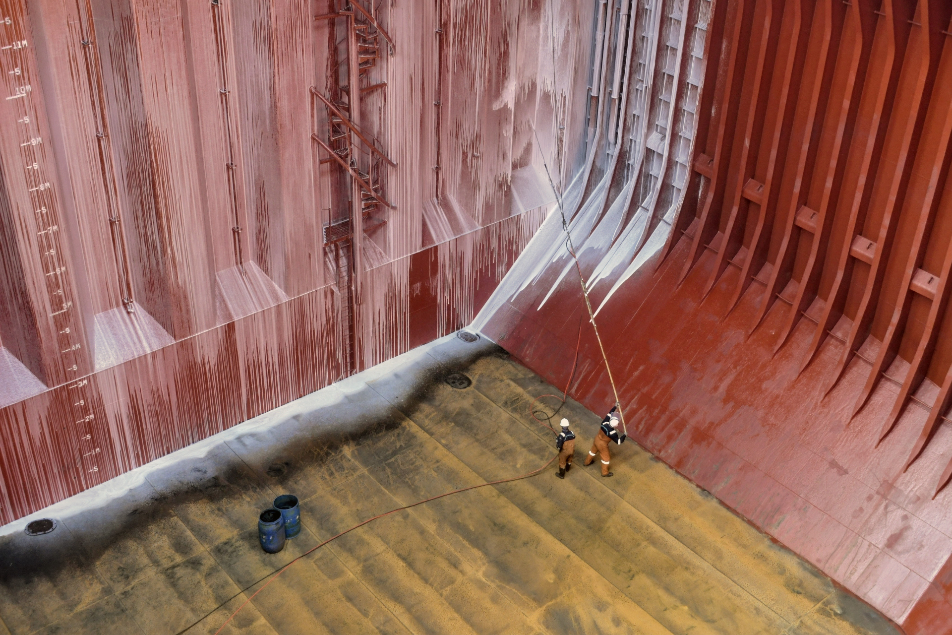 Pressure-washer spraying down the red interior wall of a bulk carrier hold