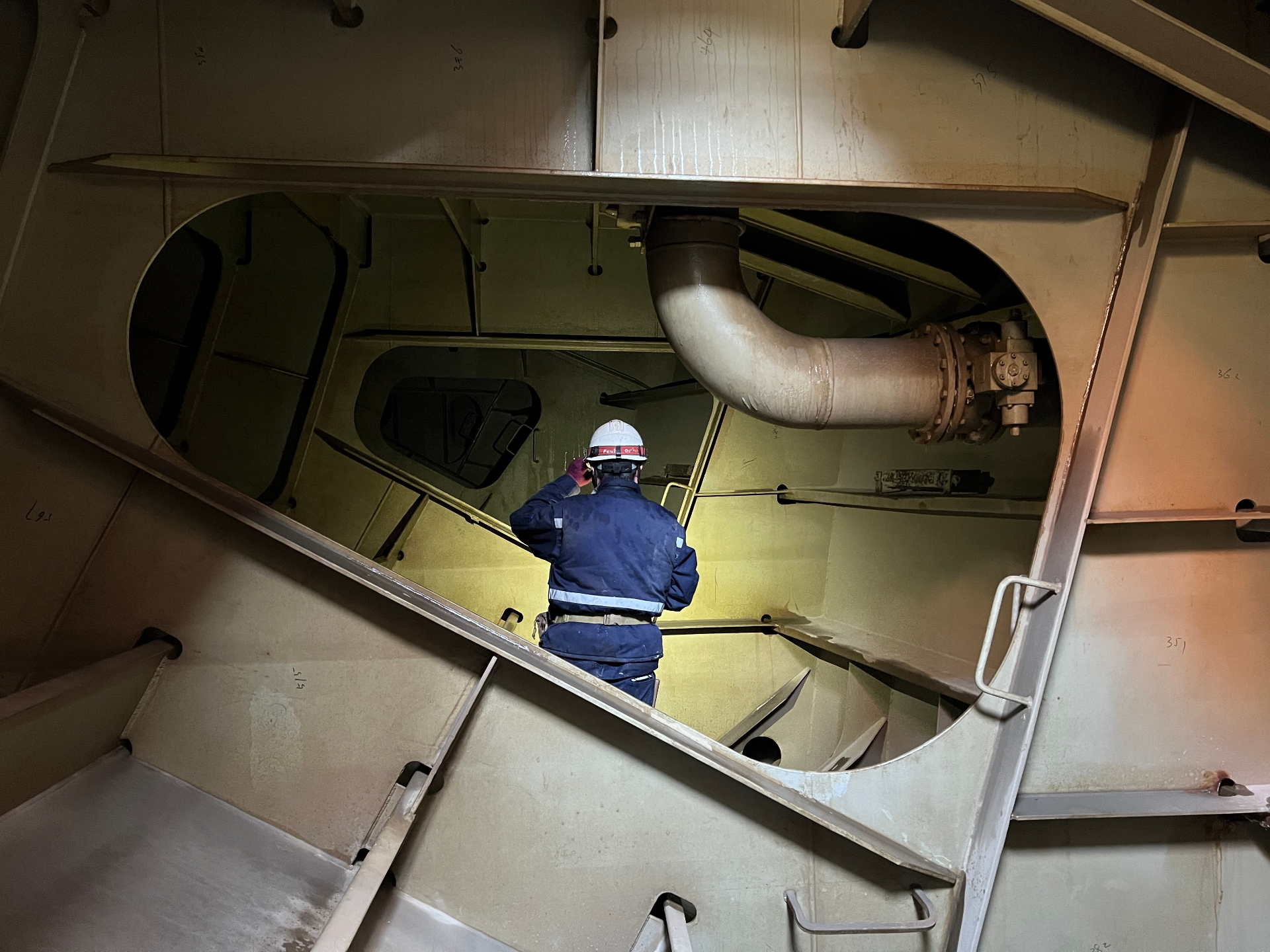 Marine technician inspecting a ship's fuel tank interior with a large pipe overhead