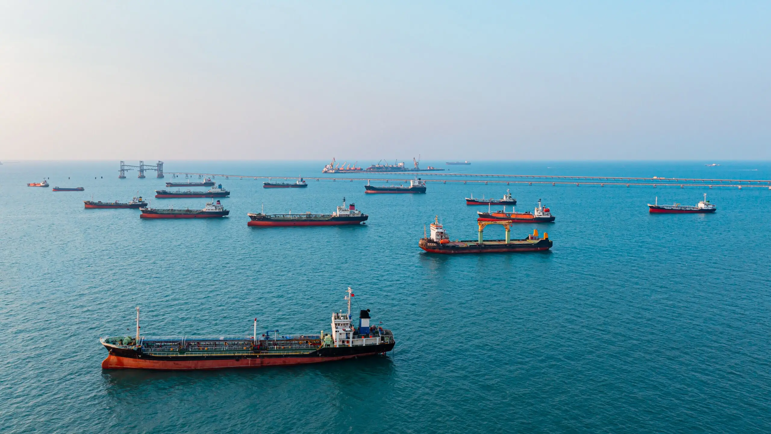 Aerial view of a sheltered anchorage with more than a dozen tankers and bulk carriers lying at anchor.